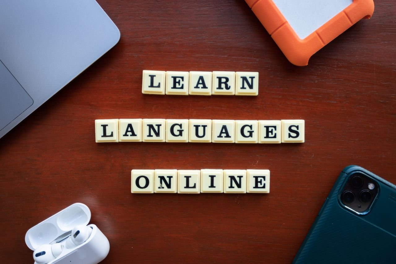 Flat lay of language learning tools with devices and text blocks on desk.